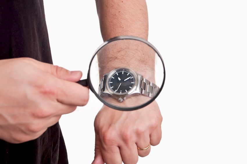 Lupe nimmt eine Armbanduhr unter die Lupe um die Wartungsbedürftigkeit zu prüfen